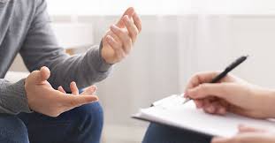 Person discussing while another writes notes.